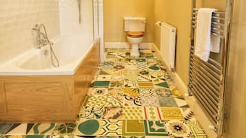 Casa de banho com banheira, sanita e chuveiro. O chão tem um padrão de mosaicos coloridos.