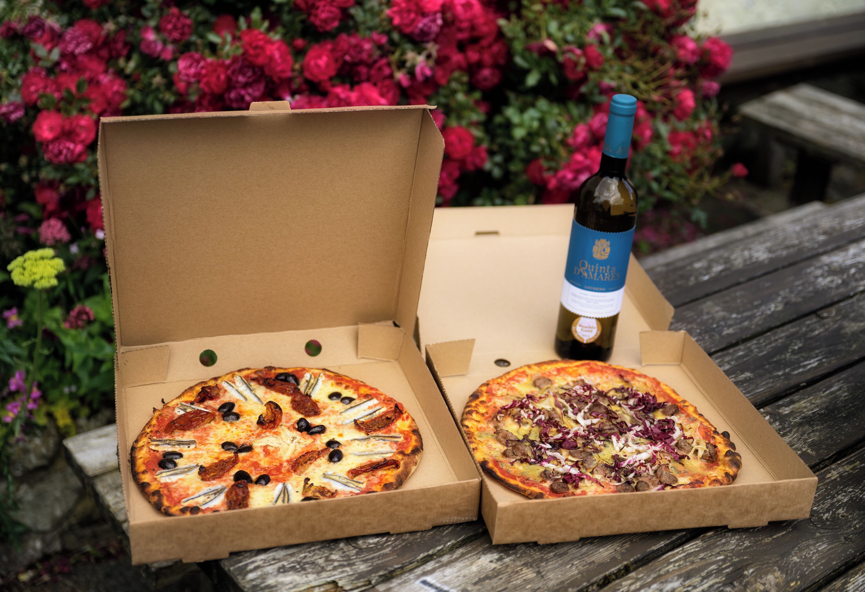 Twee geopende pizzadozen op een houten oppervlak, met een fles wijn op de achtergrond.