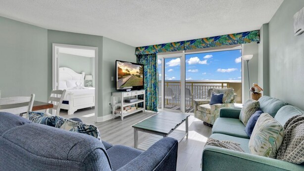 A hotel room with a balcony, a bed, a TV, a coffee table, and a sofa. - Baywatch Resort Incredible Oceanfront Family Dream Maker (North Myrtle Beach)
