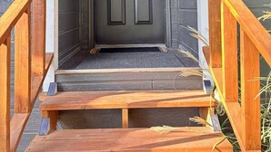 A dark wooden door with a simple handle, a small porch with a wooden railing, and a light fixture above the door. - Sleek Urban Retreat in Happy Valley (Happy Valley)