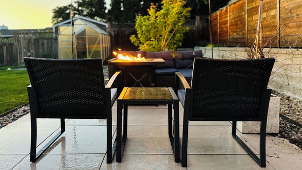 An outdoor patio with two black chairs and a table, a fire pit, string lights, and a wooden fence. - Sleek Urban Retreat in Happy Valley (Happy Valley)