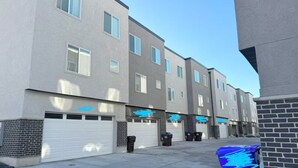 A row of modern apartment buildings with white garage doors and a blue trash bin in the foreground. - Modern Townhouse w/ All Kings and Private Rooftop (West Valley City)