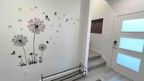 A hallway with a wall decorated with dandelion and butterfly decals, a metal rack, and a door with frosted glass panels. - Modern Townhouse w/ All Kings and Private Rooftop (West Valley City)