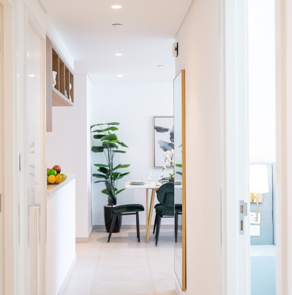 A modern, well-lit hallway with a dining area featuring a table, chairs, and a large potted plant.