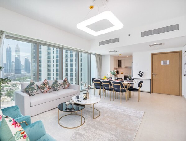 A modern living room with a sofa, coffee table, and dining area. - Vogue, Downtown with Easy Access to Dubai Mall (Dubai)