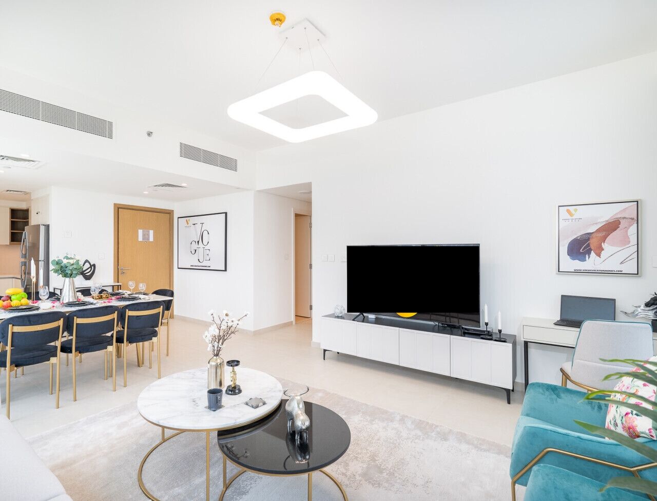 A modern living room with a flat-screen TV, a dining area with a round table, and a sofa.
