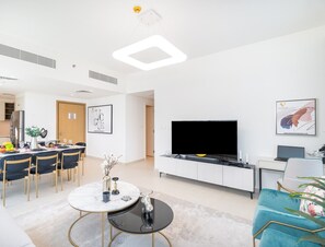 A modern living room with a flat-screen TV, a dining area with a round table, and a sofa. - Vogue, Downtown with Easy Access to Dubai Mall (Dubai)