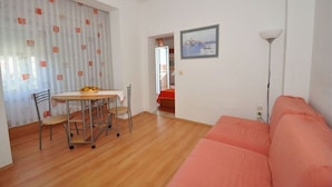 Ein Zimmer mit Holzboden, einem rosafarbenen Sofa, einem Esstisch mit Stühlen und einem Bild an der Wand.
