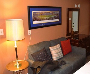A hotel room with a grey sofa, a framed picture on the wall, a lamp, and a dresser.