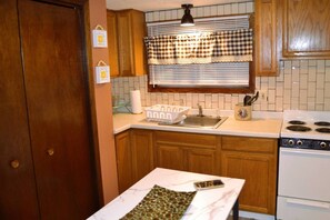A kitchen with wooden cabinets, a white countertop, a stove, and a window with a checkered valance.
