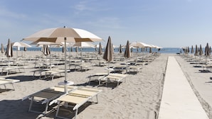A beach with rows of sun loungers and umbrellas, a clear sky, and a sandy walkway.