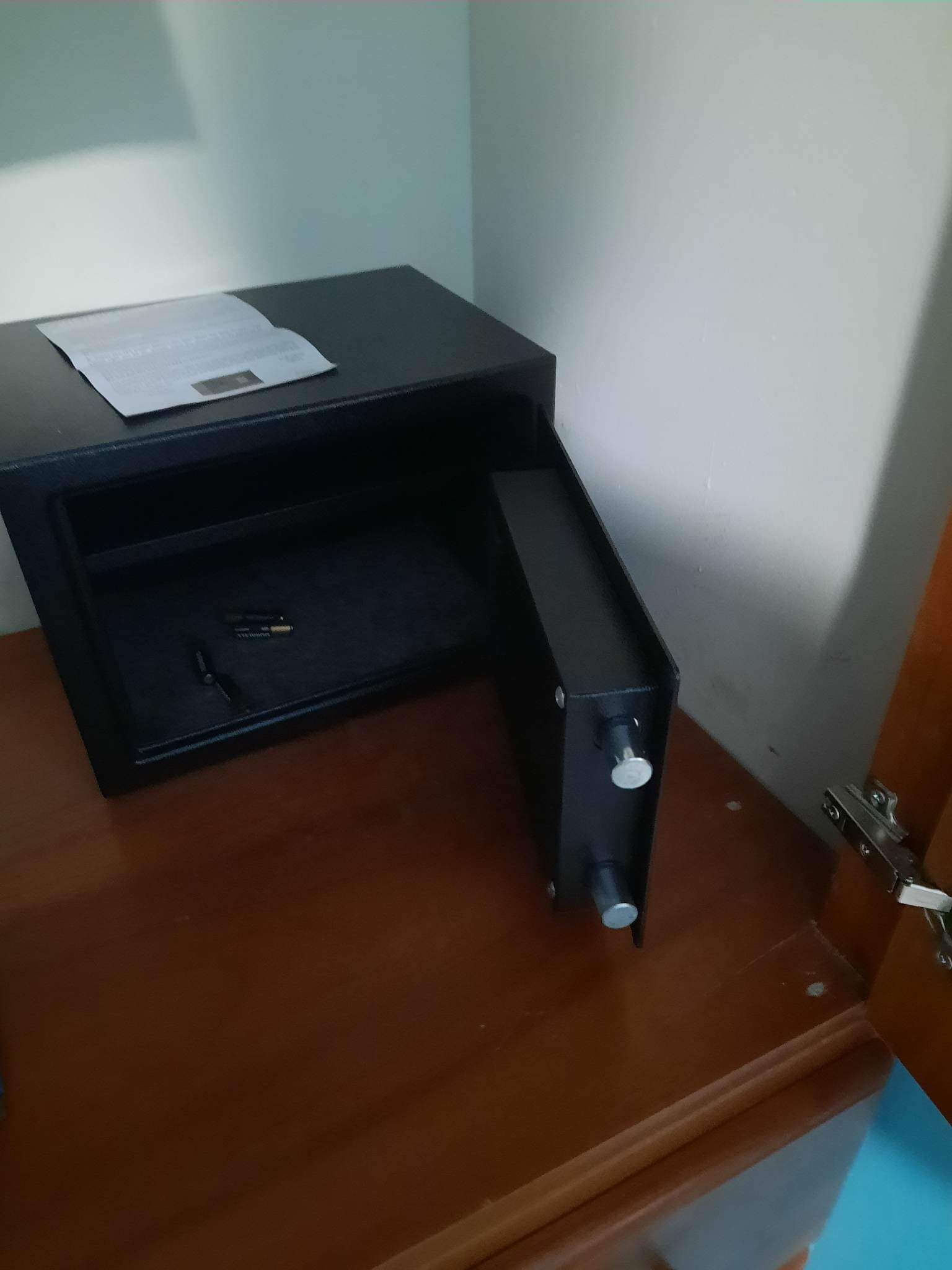 A wooden desk with a black drawer unit, a paper on top, and a pen inside the drawer.