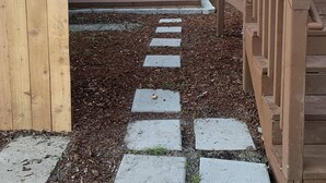 Ein Garten mit einer Holzterrasse, einem Betonweg und einem Tisch mit Stühlen.