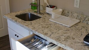 A kitchen with a marble countertop, a sink, a dish rack, and a drawer with utensils. - Judkins Guesthouse (Close to Downtown) (Seattle)