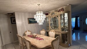 Un comedor con una mesa grande, sillas, una araña y un aparador con vidrio que exhibe objetos decorativos.