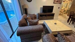 Una sala de estar con un juego de sofá, televisión y un comedor con sillas y una mesa.