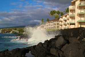 A coastal hotel with balconies, a rocky shoreline, and palm trees. - Sea Village (Kailua-Kona)