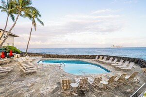 Zona junto a la piscina con sillones reclinables y una piscina, con vistas al océano y un crucero al fondo.