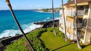 A beachfront hotel with a well-maintained lawn, balconies with railings, and a view of the ocean. - Sea Village (Kailua-Kona)