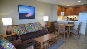 A living room with a sofa, chairs, a coffee table, and a dining table. There is a kitchen area with cabinets and appliances. - Sea Village (Kailua-Kona)