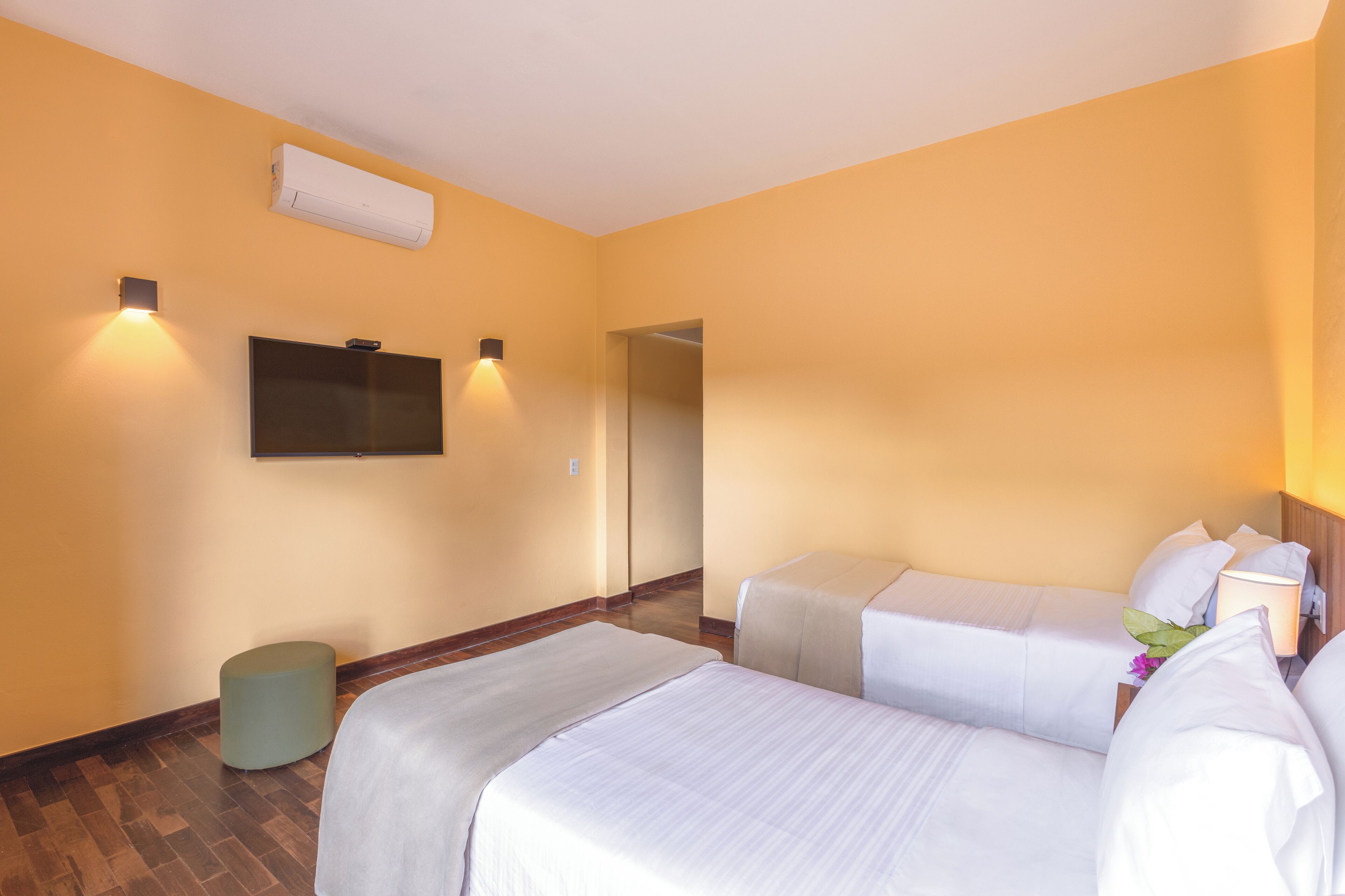 Une chambre d’hôtel avec deux lits, un téléviseur à écran plat fixé au mur et un appareil de climatisation.