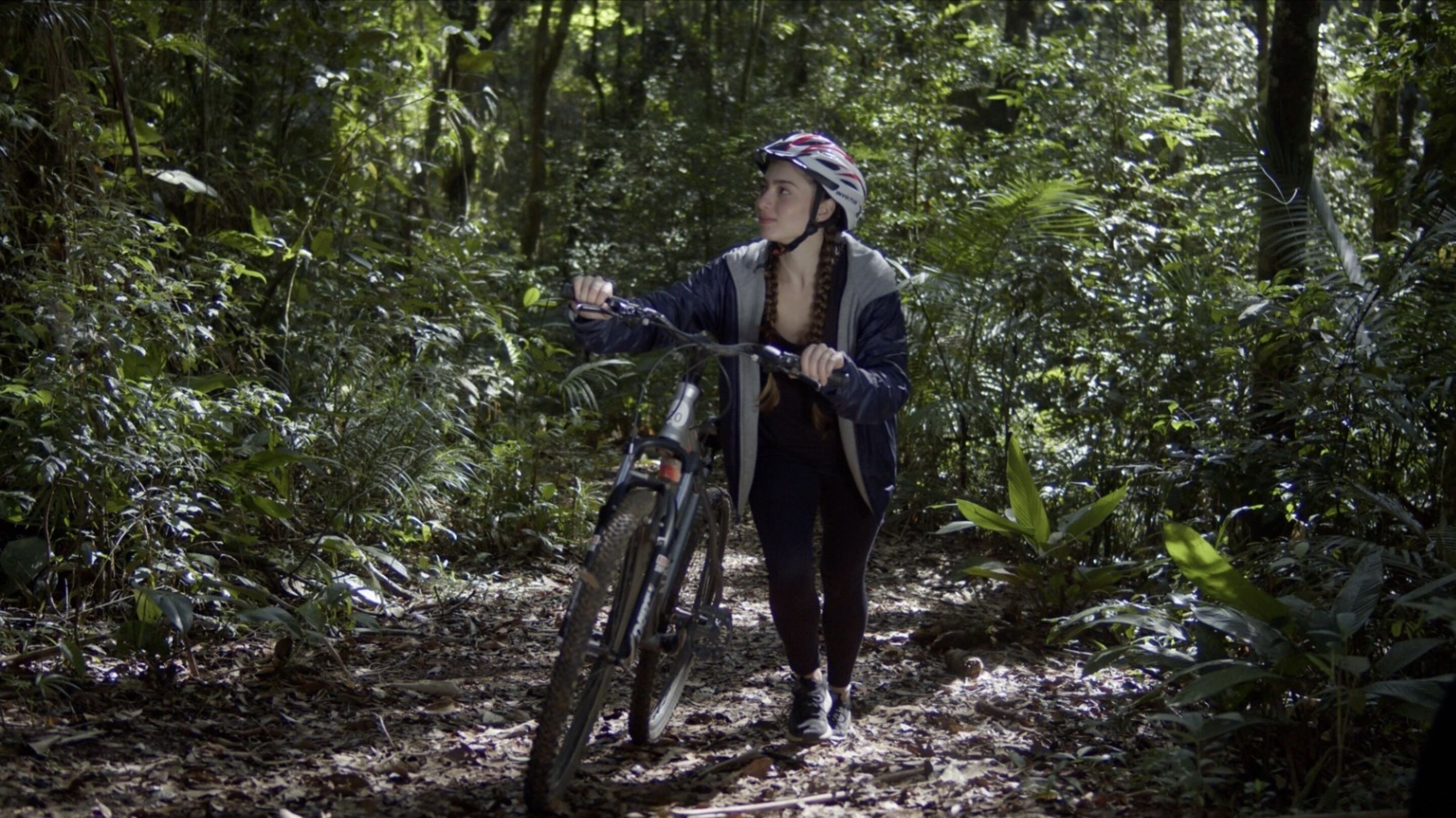 A person walking a bicycle through a forested area.