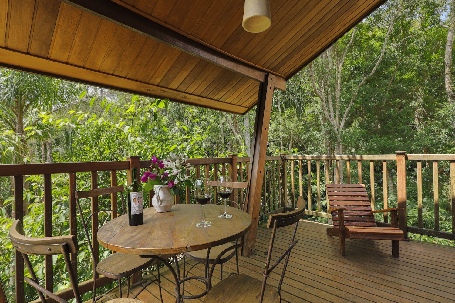 A wooden deck with a table and chairs, surrounded by lush greenery.