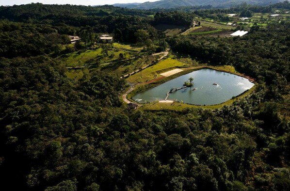 An aerial view of a lush, green landscape with a large pond surrounded by dense forest. - Hotel Fazenda Morros Verdes Ecolodge (Ibiuna)