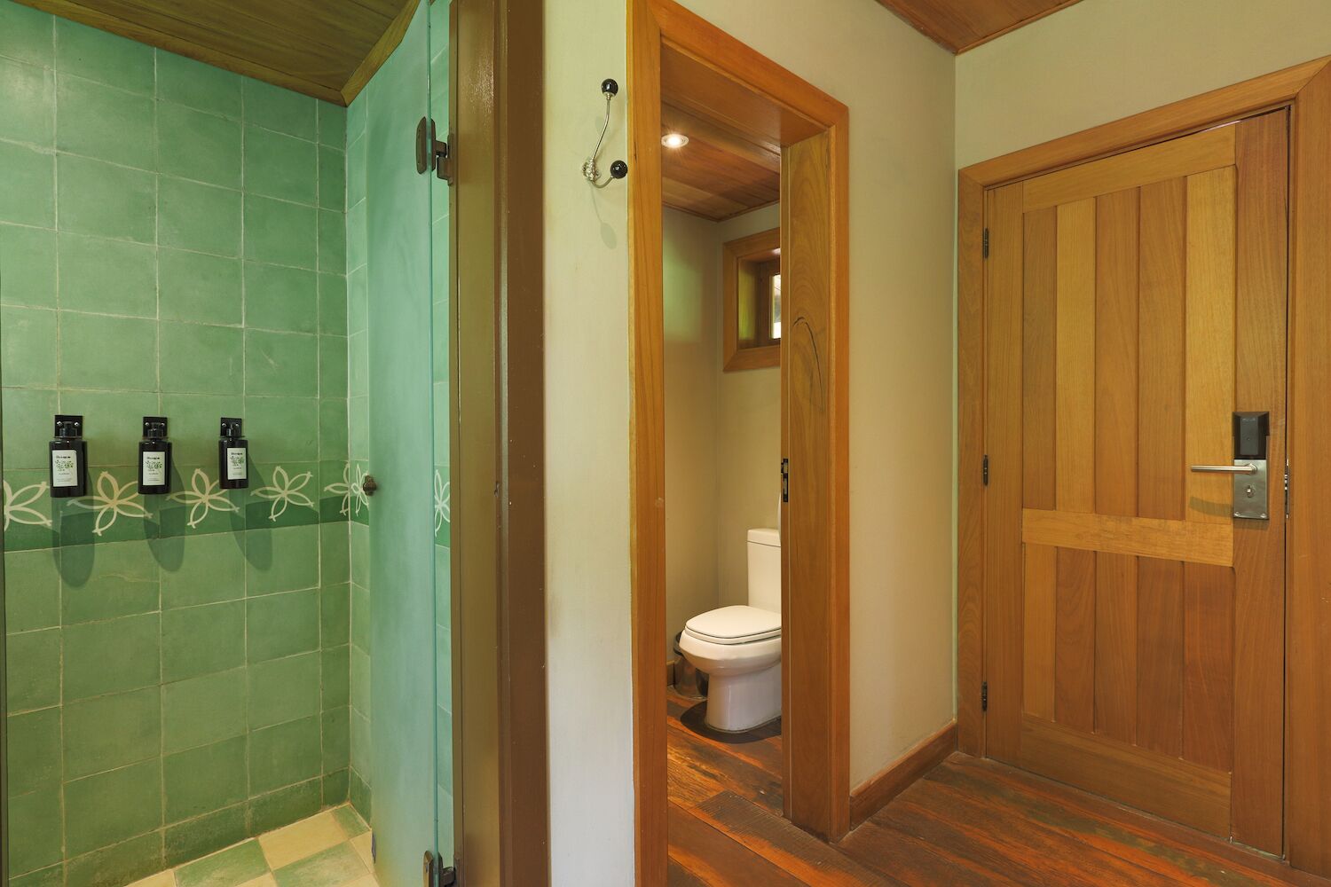 Un baño con azulejos verdes, una puerta de madera y un inodoro.