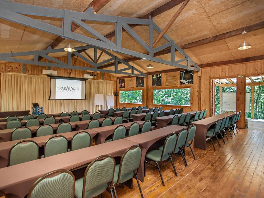 A conference room with long tables and chairs, wooden beams on the ceiling, and a projector screen displaying "SAINTURA".
