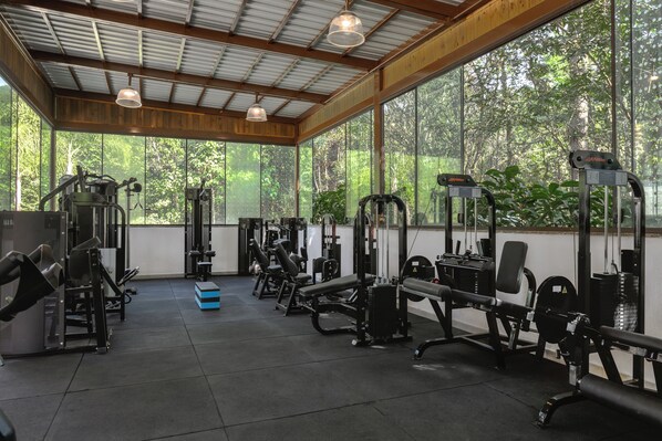 Un gimnasio con diverso equipamiento de ejercicio, amplias ventanas y techo de madera.