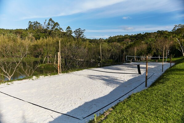 Una cancha de voleibol de arena con red, rodeada de árboles y una masa de agua.