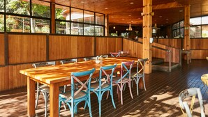A wooden interior with a large dining table and chairs, a staircase, and large windows.
