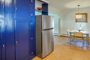 A kitchen with a stainless steel refrigerator, a blue cabinet, a dining table with chairs, and a window with a hanging light fixture. - Windham Home Near Mountain Biking & Hiking Trails! (Windham)