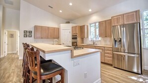 A modern kitchen with wooden cabinets, a stainless steel refrigerator, and a central island with bar stools. - Waterfront Oasis and Boaters Paradise! Coastal style home with Boat Dock! 🚤🎣 (Englewood)