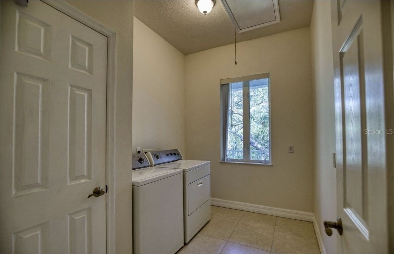 A laundry room with a washer and dryer, a window with a view of trees, and a door.