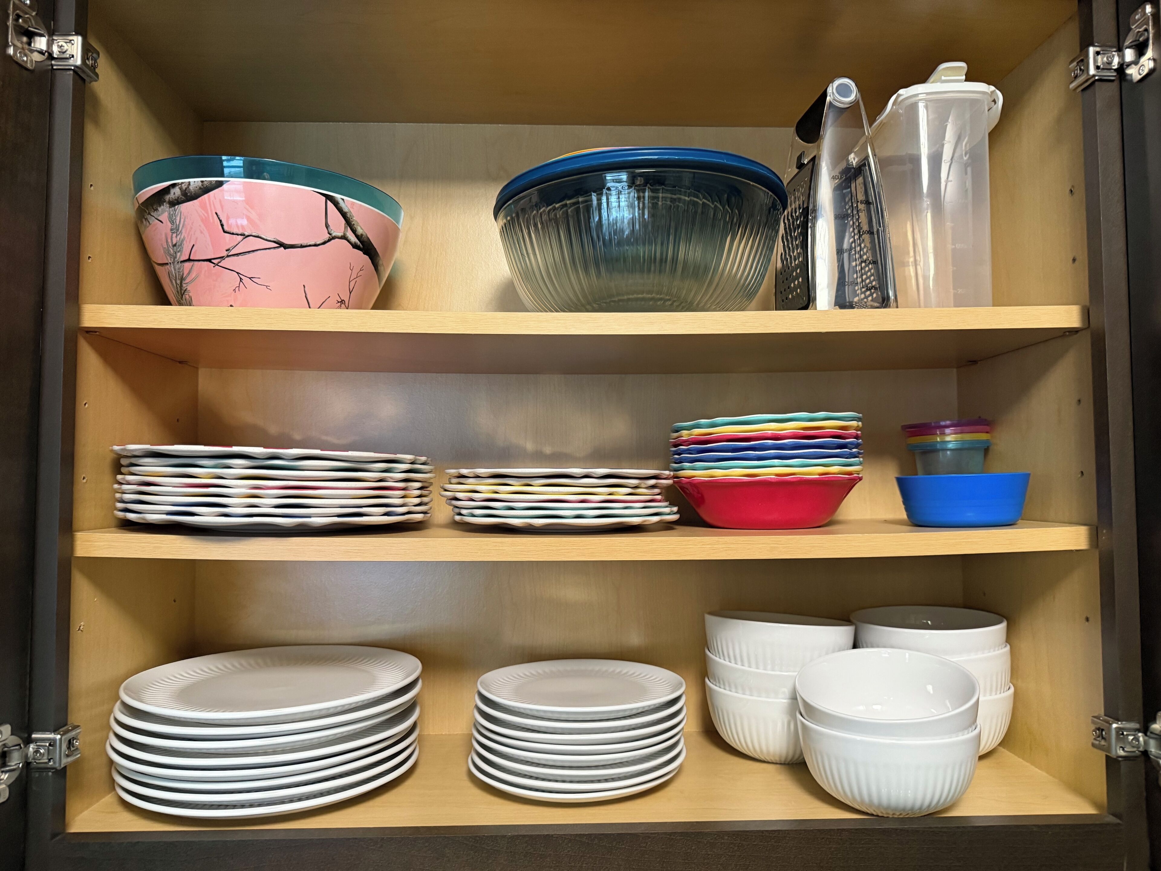 A kitchen cabinet with neatly stacked plates, bowls, and a colander.
