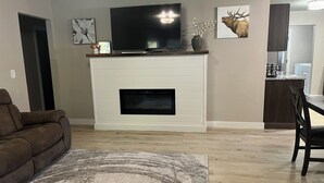 A living room with a fireplace, a television, and a dining area with a chair and table.