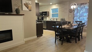 A modern kitchen with a dining area, wooden flooring, and a fireplace.