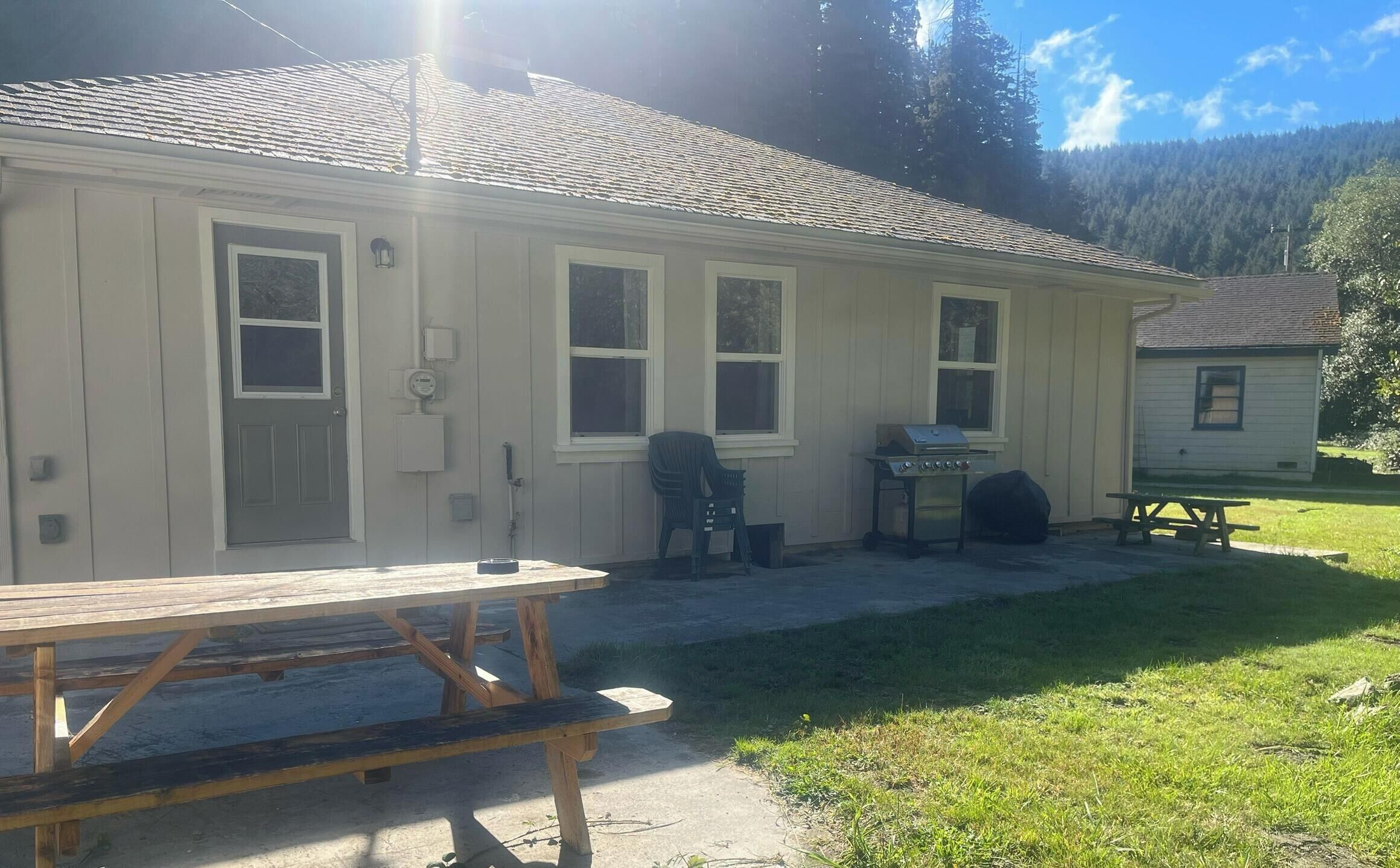 A single-story house with a front porch, a barbecue grill, and a picnic table.