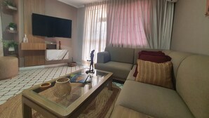 A modern living room with a sofa, a coffee table, a flat-screen TV, and a large window with curtains. - Apartahotel de lujo en Barranquilla x5 personas - Apto 301 (Barranquilla)