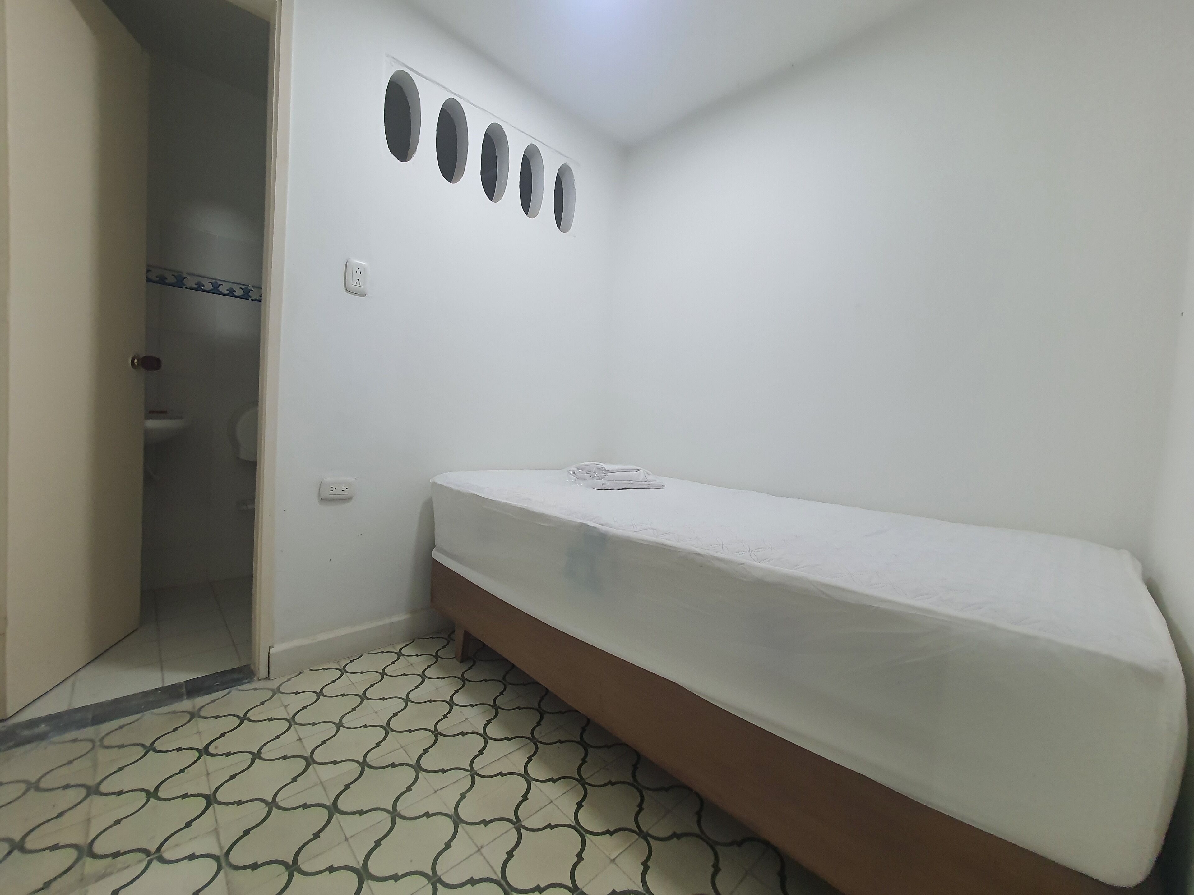 Habitació petita i blanca amb un llit individual, un vàter i un rentapeus.