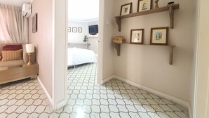 A hotel room with a bed, a TV, a shelf with pictures, and a patterned floor. - Apartahotel de lujo en Barranquilla x5 personas - Apto 301 (Barranquilla)