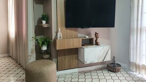 A modern living room with a flat-screen TV mounted on a wooden panel, a small white table with a decorative item, and a potted plant on a shelf. - Apartahotel de lujo en Barranquilla x5 personas - Apto 301 (Barranquilla)