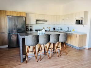 A modern kitchen with a central island, bar stools, stainless steel appliances, and wooden cabinetry.