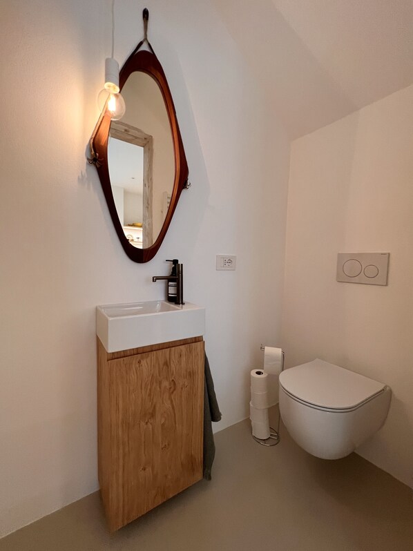 A modern bathroom with a wooden vanity, a round mirror, and a white toilet.
