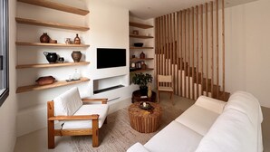 Una sala de estar moderna con estantes de madera, un televisor de pantalla plana, un sofá blanco, una silla de madera y una escalera con barandillas de madera.
