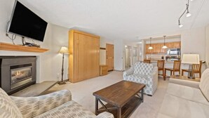 A living room with a fireplace, patterned sofas, a wooden coffee table, and a television mounted on the wall. - The Wren Studio VAIL WALK toLIFT (Vail)