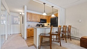 A modern kitchen with wooden cabinets, a black refrigerator, and a central island with chairs. - The Wren Studio VAIL WALK toLIFT (Vail)