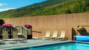 A swimming pool with lounge chairs and a wooden fence, surrounded by greenery and hills. - The Wren Studio VAIL WALK toLIFT (Vail)